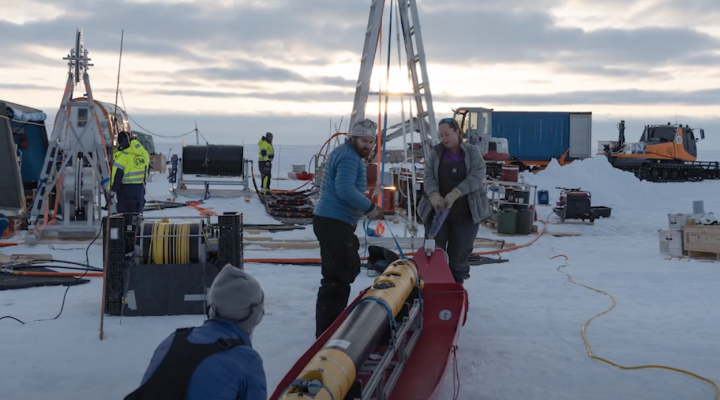 the Icefin underice robot sits on the ice with several researchers working to deploy it.