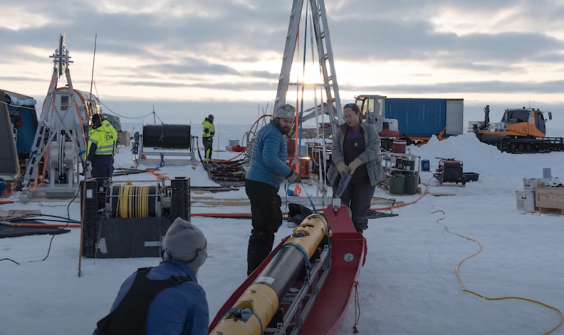 the Icefin underice robot sits on the ice with several researchers working to deploy it.